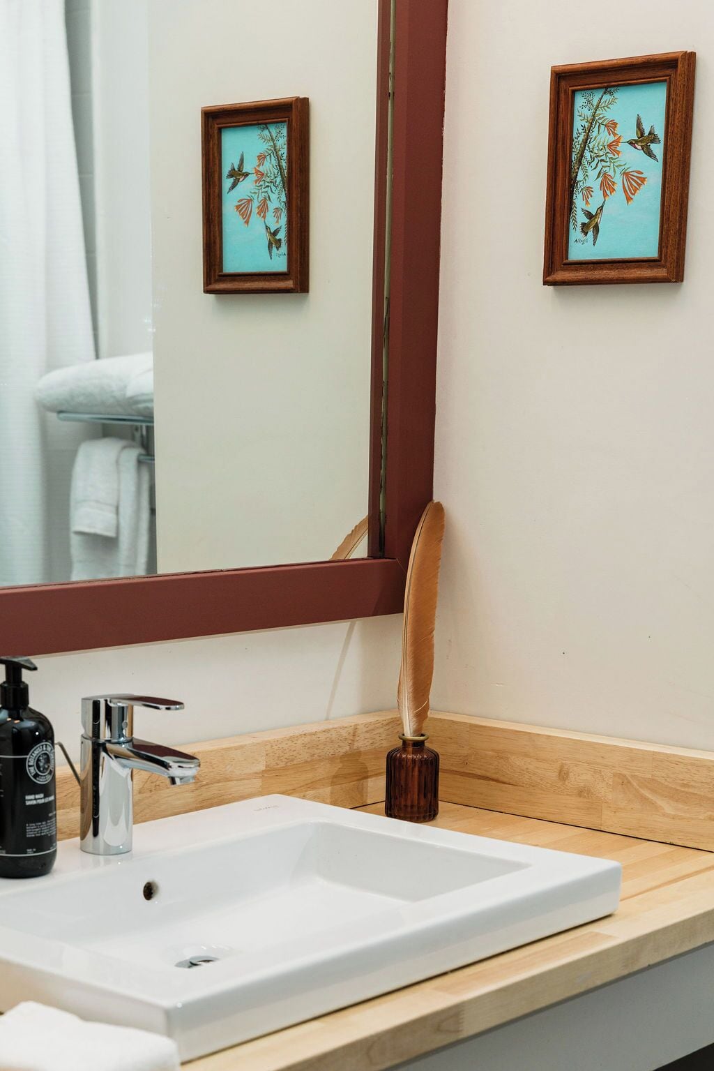 A bathroom with a white sink, a mirror, and two framed artworks on the wall.