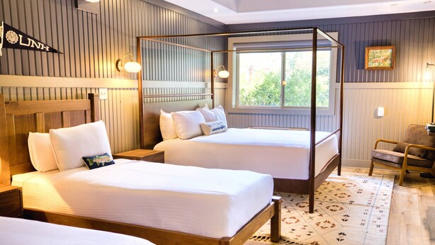 A hotel room with two beds, a canopy bed, a wooden headboard, a chair, a window, and a wall-mounted sign. - Hideaway Inn Mt.Sunapee (Newbury)