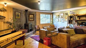 A cozy living room with a stone fireplace, wooden benches, a leather sofa, and a bookshelf filled with books and decorative items. - Hideaway Inn Mt.Sunapee (Newbury)
