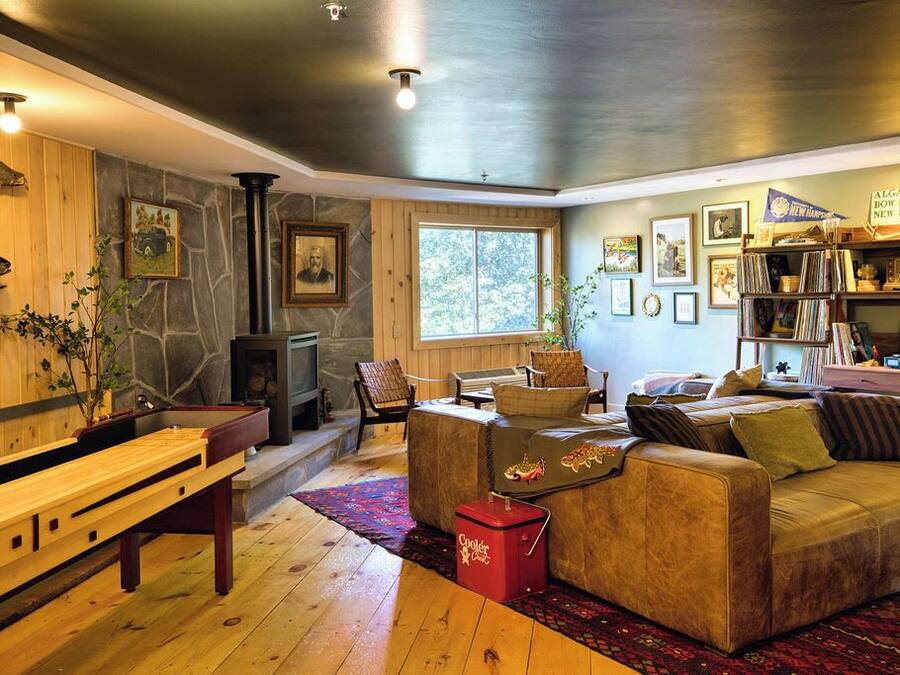 A cozy living room with a stone fireplace, wooden benches, a leather sofa, and a bookshelf filled with books and decorative items.