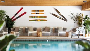 A poolside area with a wooden ceiling, a seating arrangement with chairs and cushions, and skis and snowboards on the wall. - Hideaway Inn Mt.Sunapee (Newbury)