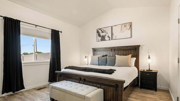 Une chambre à coucher avec un lit en bois, un banc, une table de chevet et une fenêtre avec des rideaux.