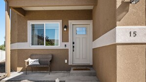 Une entrée d’immeuble avec une porte blanche, un banc doté d’un coussin et le chiffre « 15 » peint sur le mur.