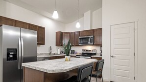 Une cuisine moderne dotée d’appareils électroménagers en acier inoxydable, de meubles en bois, d’un îlot en marbre et de luminaires suspendus.