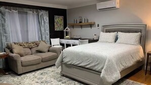 A bedroom with a large bed, a sofa, a desk, and an air conditioning unit. - Cottage Studio Suite # 1 (Fort Payne)