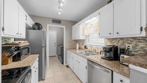 Una cucina moderna con mobili bianchi, piani di lavoro in granito, elettrodomestici in acciaio inossidabile e una finestra con tende.