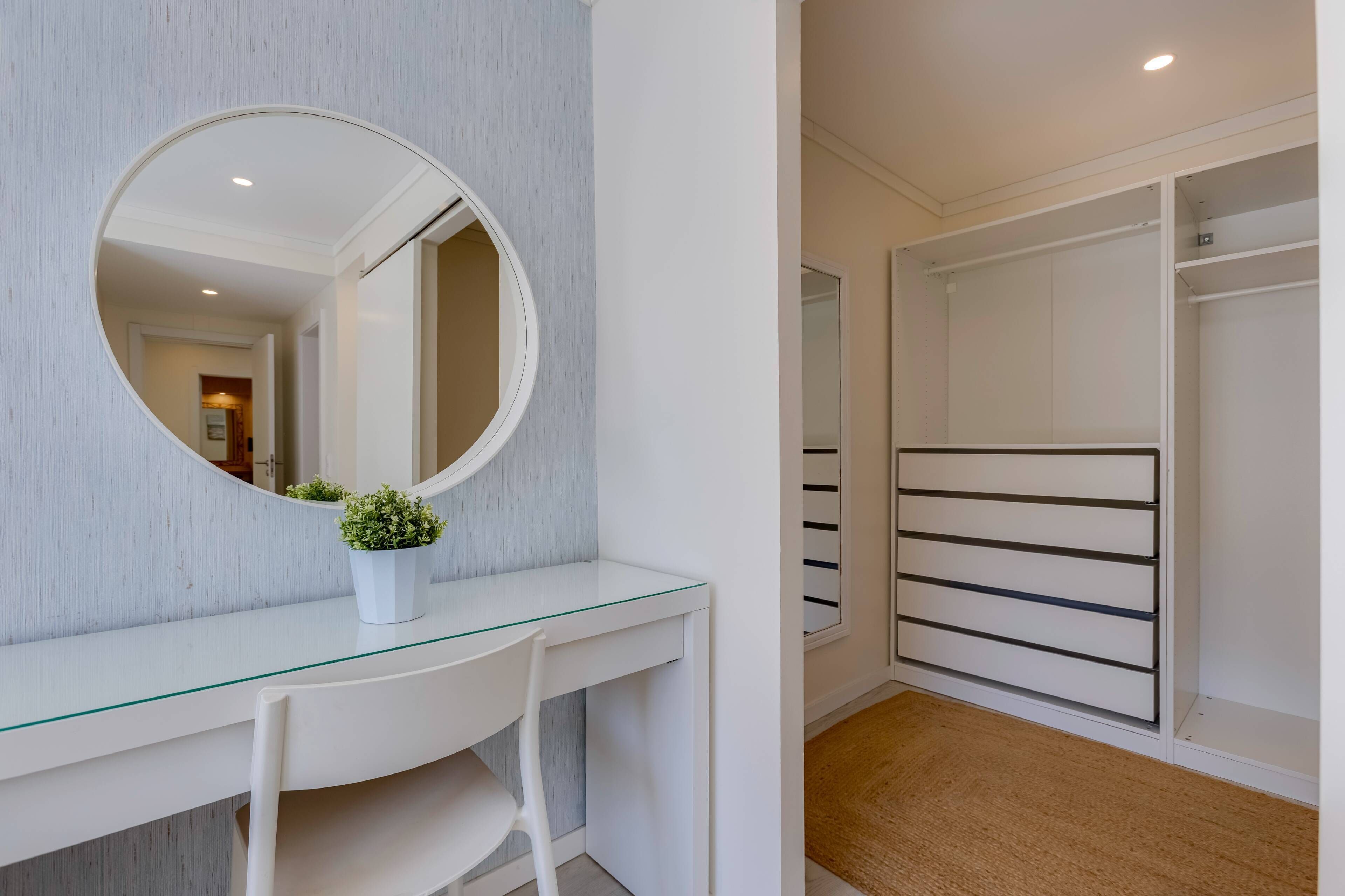A modern bathroom with a glass vanity, a round mirror, and a white storage unit.