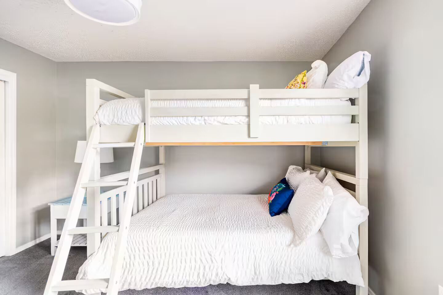 A bunk bed room with a ladder, white bedding, and a pillow with a floral design.