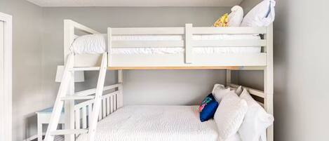 A bunk bed room with a ladder, white bedding, and a pillow with a floral design.