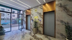 Un hall d’entrée moderne avec un sol en marbre, des portes en verre, des ascenseurs et une plante en pot.