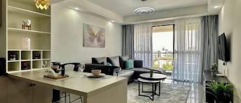 A modern living room with a sofa, a coffee table, and a dining area with a kitchen counter.
