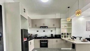 Une cuisine moderne avec un sol en marbre gris, des meubles blancs et un réfrigérateur noir.
