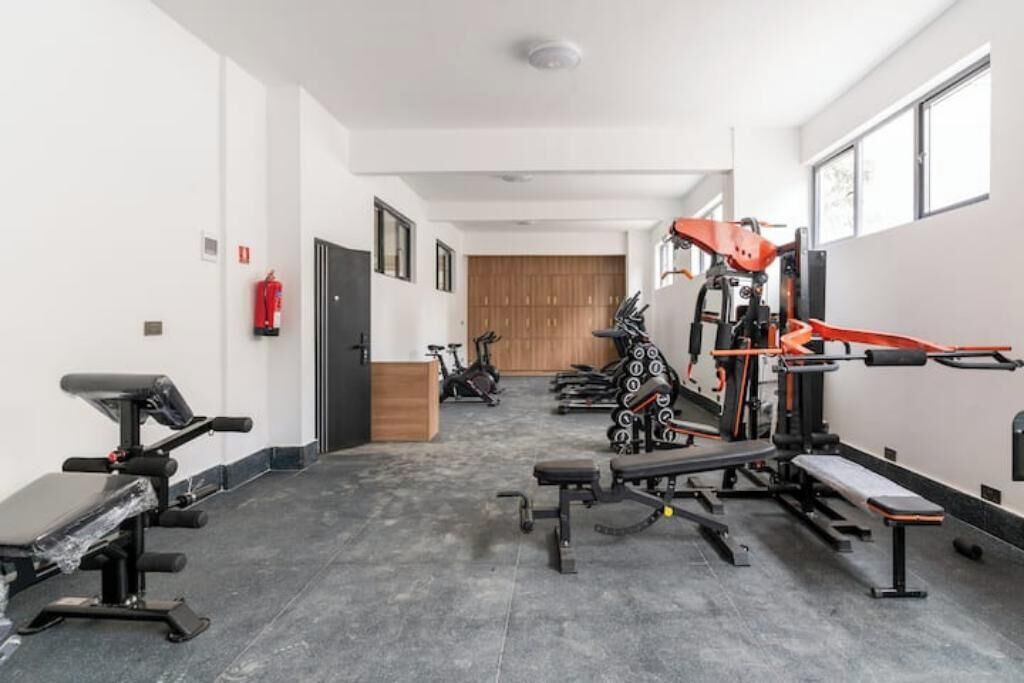 A gym with various exercise equipment, a fire extinguisher, and a wooden door in the background.