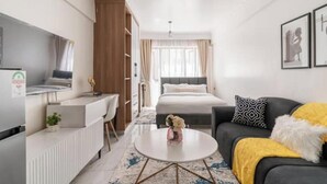 A modern hotel room with a bed, a sofa, a desk, and a TV.