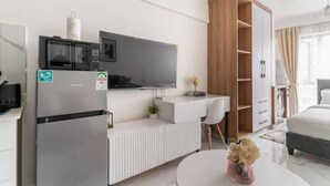 A modern hotel room with a kitchenette, a flat-screen TV, a wooden wardrobe, a desk, and a bed.