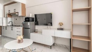 A modern kitchen with white cabinetry, a built-in microwave, and a large flat-screen TV.