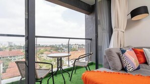 A balcony with a view of a cityscape, a sofa with colorful cushions, and a small table with chairs. - Linden Lane Hideaway Gym,Heated Pool & City Views (Nairobi)