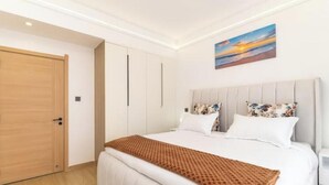 A hotel room with a bed, a nightstand, a painting on the wall, and a wooden door. - Linden Lane Hideaway Gym,Heated Pool & City Views (Nairobi)
