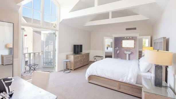 Une chambre d’hôtel spacieuse, dotée d’un grand lit, d’une télévision, d’un bureau avec une chaise et d’un balcon offrant une vue agréable.