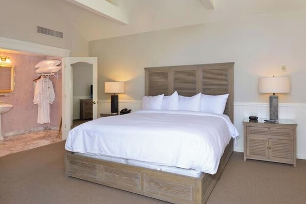 A neatly arranged bedroom with a large bed, bedside tables, a wardrobe, and a bathroom visible through an open door.