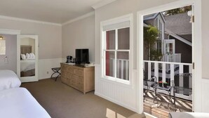 Hotelkamer met twee bedden, een kapstok, een televisietoestel en een balkon met buitenmeubilair.