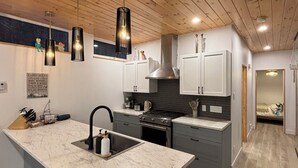 A modern kitchen with a marble island, stainless steel appliances, and wooden ceiling beams. - Summit Living Redefined: Alpine Views, Forest Serenity,5 Minutes from everything (Saint Donat)