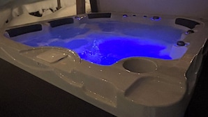 A hot tub with a blue light, wooden ceiling beams, and a snowy outdoor area. - Summit Living Redefined: Alpine Views, Forest Serenity,5 Minutes from everything (Saint Donat)