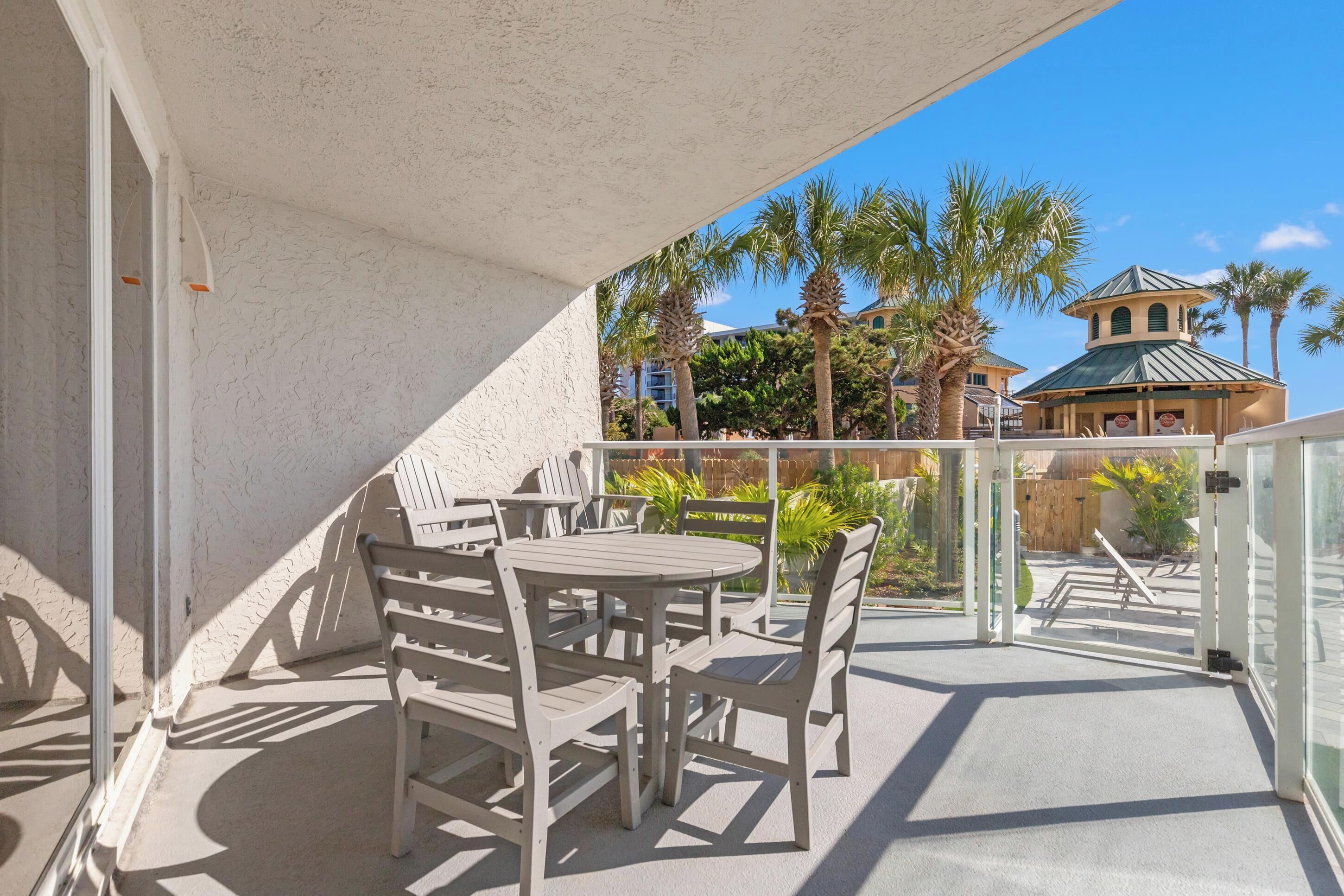 A balcony with white chairs and tables, a view of palm trees and a building with a green roof.