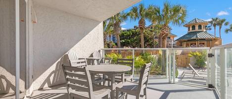 A balcony with white chairs and tables, a view of palm trees and a building with a green roof.