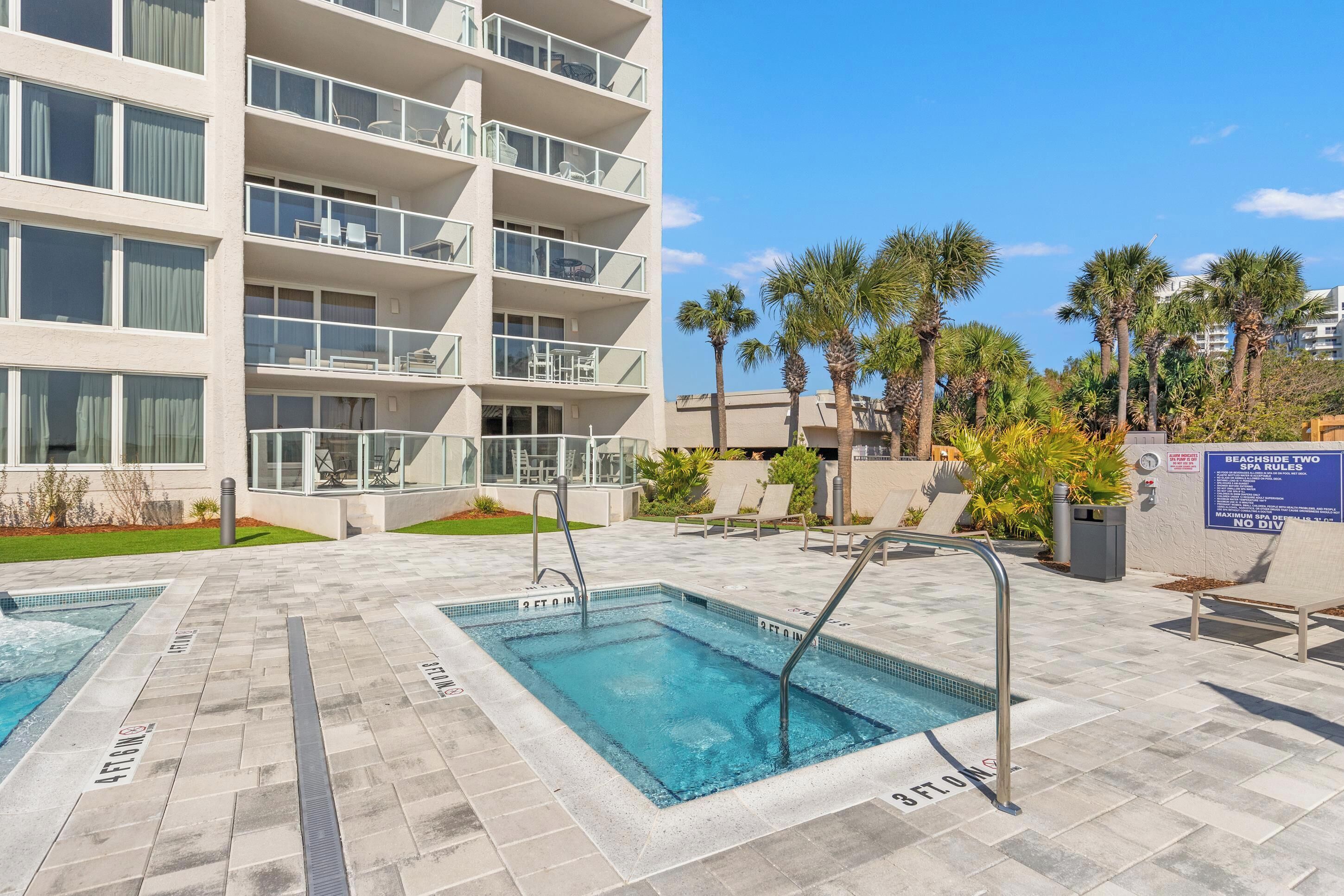 A pool area with two rectangular pools, a multi-story building with balconies, and palm trees.