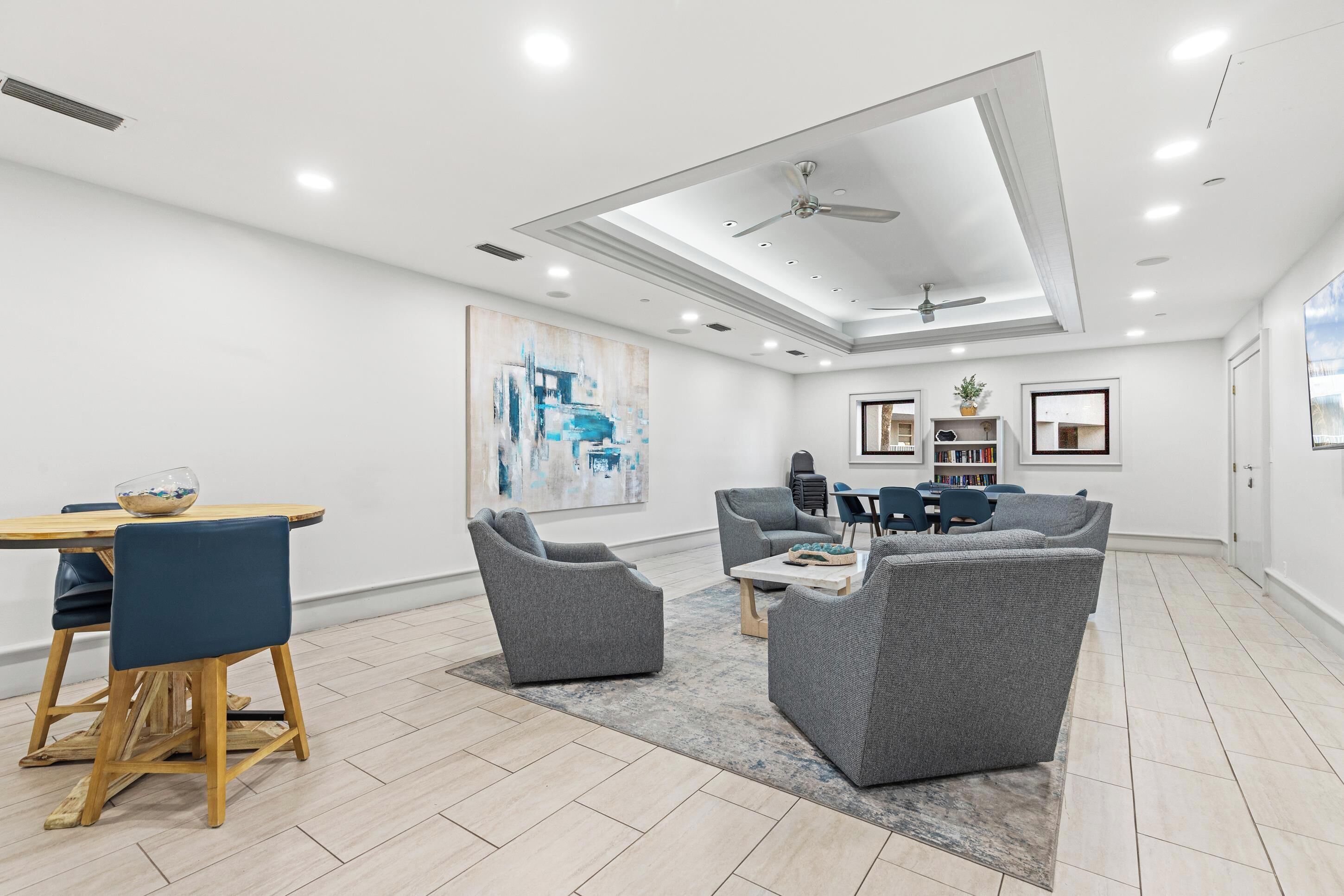 A spacious living room with a dining area, grey upholstered furniture, a ceiling fan, recessed lighting, and a large abstract painting on the wall.