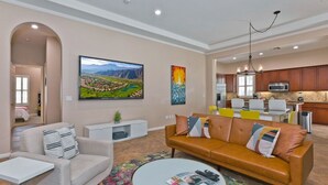Una sala de estar moderna con un sofá, un sillón y una mesa de centro. Se ve una cocina al fondo con un comedor.