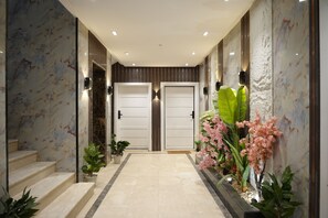 A hallway with marble walls, two white doors, and potted plants. - SARA Residences (Riyadh)