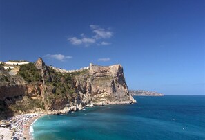 A coastal landscape with a rocky cliff, a beach, and a clear blue sea. - Villa Benitachell, La Cumbre del Sol (El Poble Nou de Benitachell)