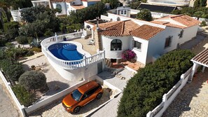 Eine Villa im mediterranen Stil mit Swimmingpool, einer gepflasterten Auffahrt und einem parkenden Auto.