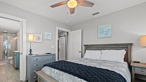 A bedroom with a bed, a nightstand, a dresser, a ceiling fan, and a door leading to another room.