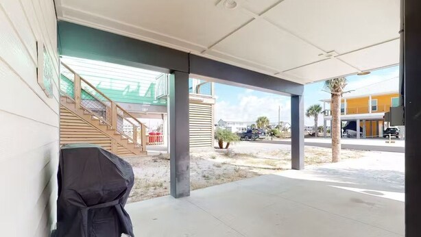 A covered outdoor area with a grill, a staircase, and a view of the street and buildings.