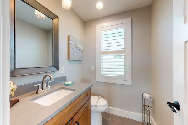 A bathroom with a large mirror, a sink, a toilet, and a window with blinds.