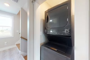 A compact laundry room with a built-in washer and dryer, a window providing natural light, and a wooden staircase leading to an upper level.