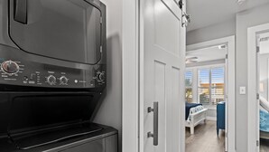 A modern kitchen with a built-in washer and dryer, a white door leading to a bedroom with a bed and a view of the outside.