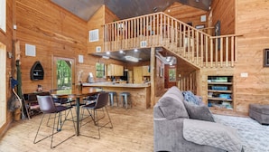 A wooden cabin interior with a dining area, kitchen, and a cozy living space with a sofa and a fireplace.