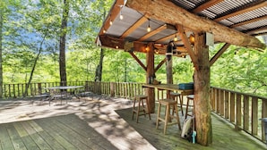 A wooden deck with a covered seating area, surrounded by trees.