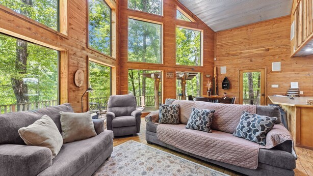 A spacious cabin with large windows, a cozy living area with a sofa and armchairs, a dining table, and a kitchen area.