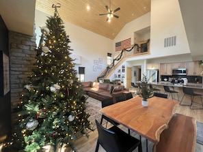 A spacious living area with a large Christmas tree, a wooden dining table, and a kitchen with modern appliances.