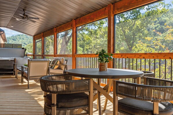 A covered outdoor deck with wooden furniture, a round table, and a potted plant.