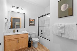 A modern bathroom with a wooden vanity, a toilet, a shower with a glass door, and a towel rack.