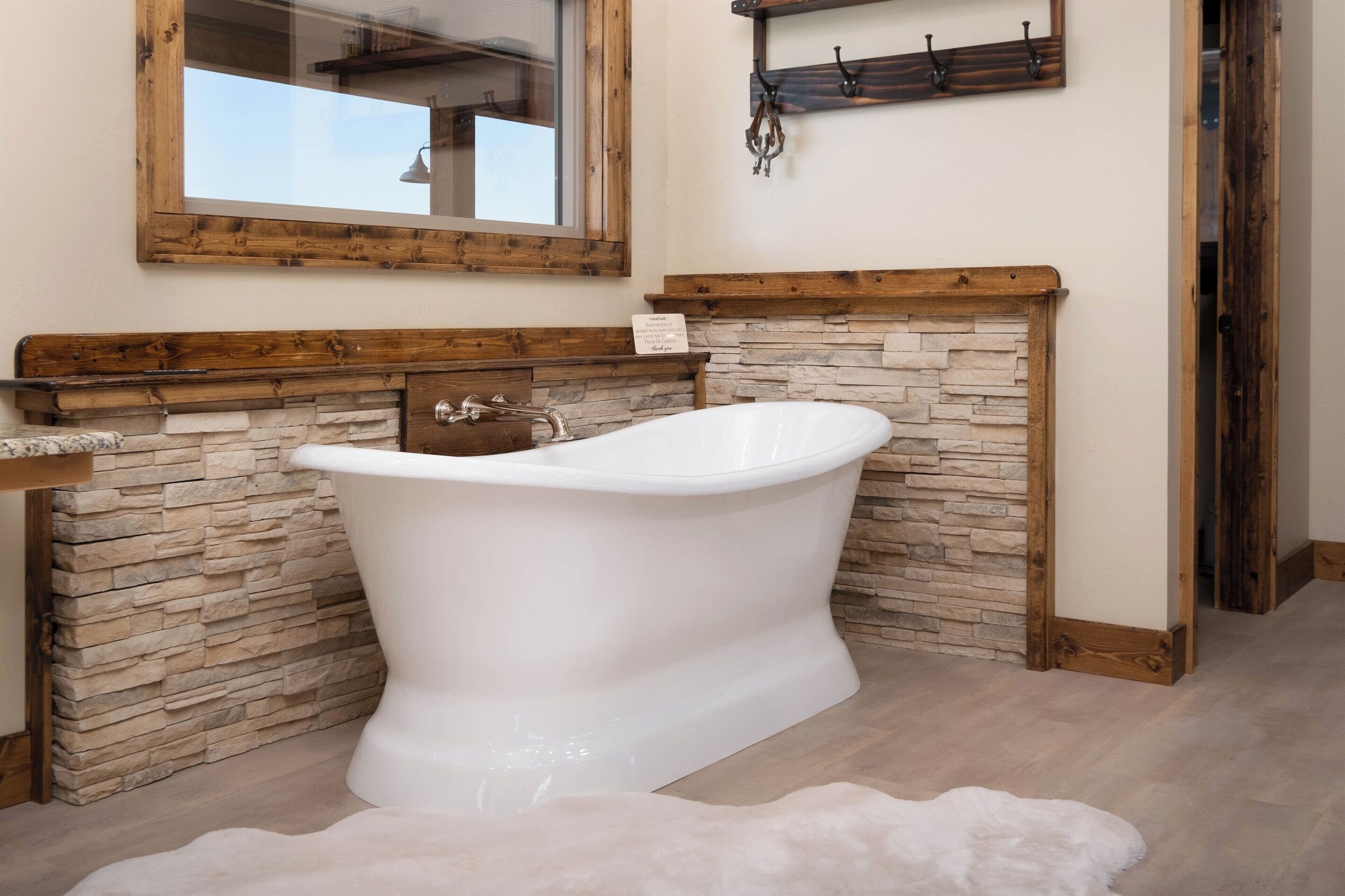 Ein Badezimmer mit freistehender Badewanne, Steinwand, Holzbalken und einem Spiegel darüber.