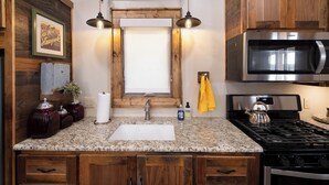 A kitchen with a granite countertop, stainless steel appliances, wooden cabinets, and a hanging light fixture.