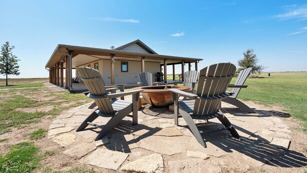 A covered outdoor area with Adirondack chairs, a fire pit, and a house in the background.