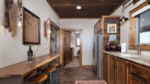 A kitchen with wooden cabinets, a stainless steel refrigerator, a bar area with stools, and a patterned rug.